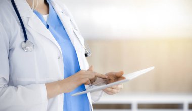 Bilinmeyen kadın doktor güneşli klinikte duruyor ve tablet bilgisayar kullanıyor, yakın plan. Veriler ve tıptaki en iyi hizmet
