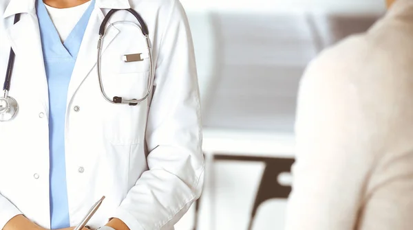 Mujer-médico desconocida y paciente en el hospital. Médico rubio controla los registros de la historia de la medicación y los resultados del examen durante el uso de portapapeles, primer plano. Concepto de medicina Fotos de stock libres de derechos