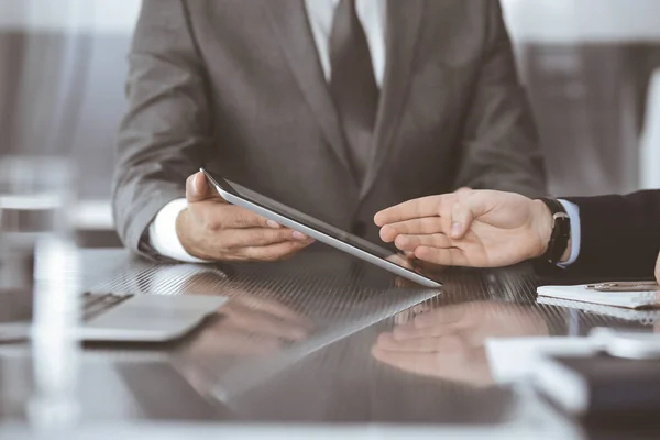 Hombre de negocios desconocido que utiliza la computadora de la tableta y el trabajo junto con su colega mientras se sienta en el escritorio de cristal en la oficina moderna. Trabajo en equipo y concepto de asociación — Foto de Stock