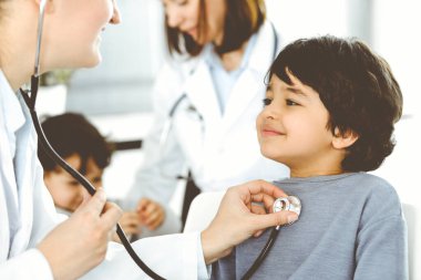 Doktor-kadın bir çocuğu steteskopla muayene ediyor. Doktor randevusunda tatlı bir Arap çocuk. Tıp konsepti