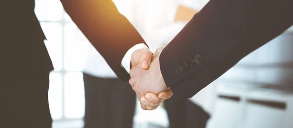 Empresario y mujer estrechando la mano con sus colegas en el fondo. Saludo en la reunión en la oficina soleada — Foto de Stock