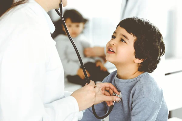 Lekarz-kobieta badający pacjenta za pomocą stetoskopu. Słodki arabski chłopiec i jego brat na wizycie u lekarza. Koncepcja medycyny — Zdjęcie stockowe