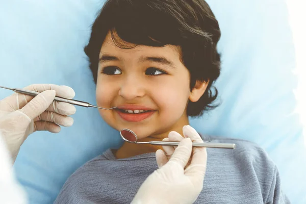 Cute chłopiec arabski siedzi na krześle dentystycznym z otwartymi ustami podczas badania doustnego z lekarzem. Odwiedzam gabinet dentystyczny. Koncepcja stomatologii — Zdjęcie stockowe