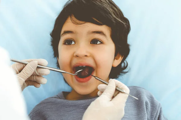 Lindo chico árabe sentado en la silla dental con la boca abierta durante el control oral con el médico. Visita al consultorio del dentista. Concepto de estomatología — Foto de Stock