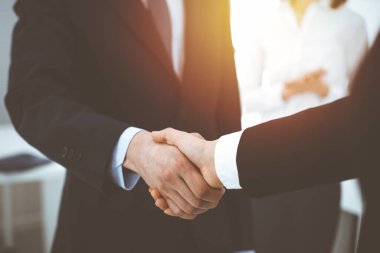 İş adamı ve kadın arka planda iş arkadaşlarıyla tokalaşıyor. Güneşli ofiste tokalaşırken