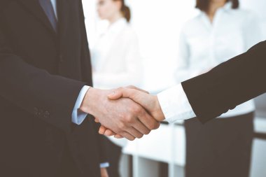 İş adamı ve kadın arka planda iş arkadaşlarıyla tokalaşıyor. Ofiste tokalaşırken. İş hayatında başarı kavramı