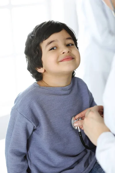 Médico-mujer examinando a un niño paciente por estetoscopio. Lindo chico árabe en la cita con el médico. Concepto de medicina — Foto de Stock