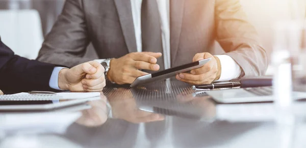 Hombre de negocios desconocido que utiliza la computadora de la tableta y el trabajo junto con su colega mientras se sienta en el escritorio de cristal en la oficina moderna. Trabajo en equipo y concepto de asociación — Foto de Stock