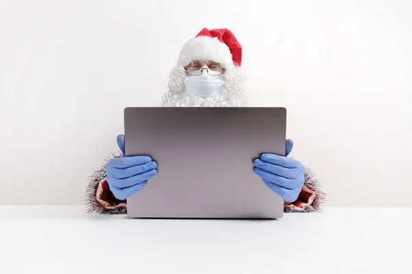 Cerrahi Maskeli Noel Baba dizüstü bilgisayarın arkasında oturuyor..