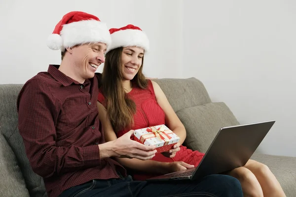 Noel Şapkalı Genç Çift, Video Çağrı ve Hediye Kutusu için dizüstü bilgisayar kullanıyor. Noel 'i evde kutluyoruz.