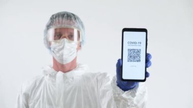 Koruyucu Takım Elbiseli Doktor Cep telefonunda Aşı Sertifikası Gösteriyor.