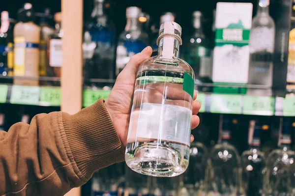 Süpermarkette alışveriş yapan bir erkek elinde bir şişe votka tutuyor.