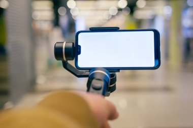 Bir adam elinde bir dengeleyiciyle akıllı telefonu tutuyor. Alışveriş merkezinde blog yazarı