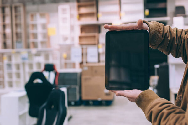 A man in a furniture store holds a tablet in his hand