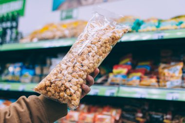 Süpermarketteki adam elinde bir torba patlamış mısır tutuyor.