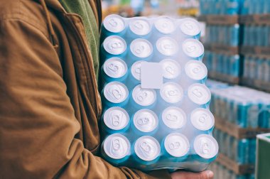 Süpermarkette alışveriş yapan biri elinde bir paket bira tutuyor.
