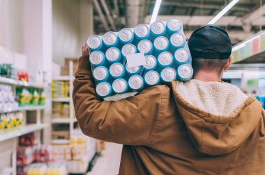 Süpermarkette alışveriş yapan biri elinde bir paket bira tutuyor.