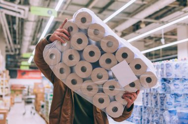 Süpermarkette alışveriş yapan biri elinde bir paket tuvalet kağıdı tutuyor.