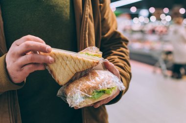 Süpermarkette bir adam hamburger ve sandviç tutuyor.