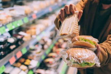 Süpermarkette bir adam hamburger ve sandviç tutuyor.