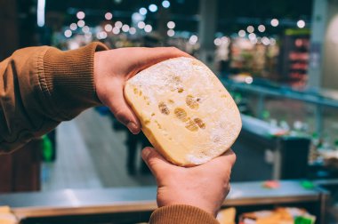 Süpermarkette elinde taze peynir tutan bir adam.