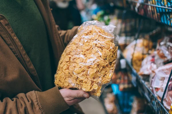 Süpermarkette bir adam elinde bir torba mısır gevreği tutuyor.