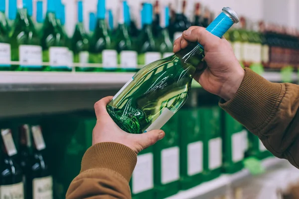 A shopper in a supermarket holds wine in his hands. Concept on the topic of selection of goods