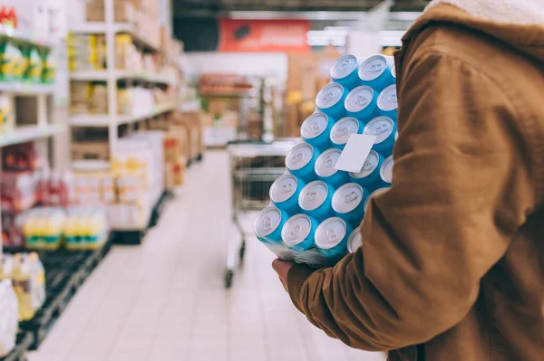 Süpermarkette alışveriş yapan biri elinde bir paket bira tutuyor.