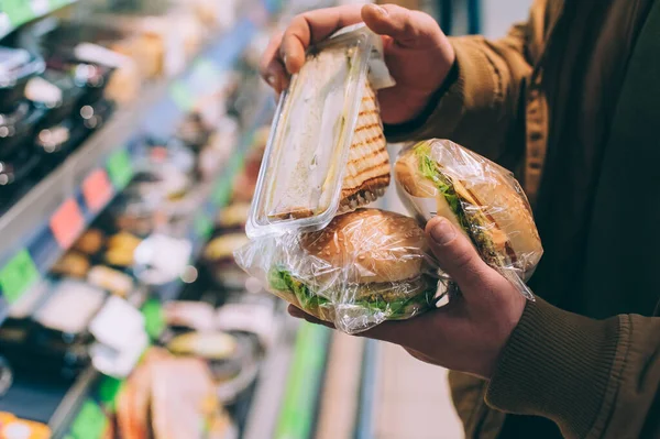 Süpermarkette bir adam hamburger ve sandviç tutuyor.
