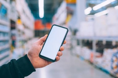 Model teknolojisi. Adam arka plandaki süpermarkette elinde akıllı bir telefon tutuyor.