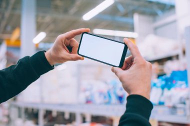 Model teknolojisi. Adam arka plandaki süpermarkette elinde akıllı bir telefon tutuyor.