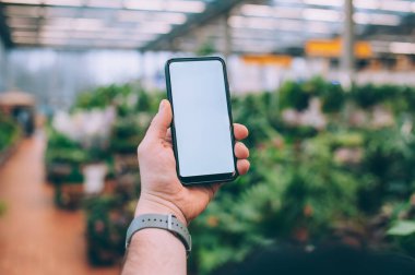 Model teknolojisi. Adam arka plandaki çiçeklerin üzerinde akıllı bir telefon tutuyor.