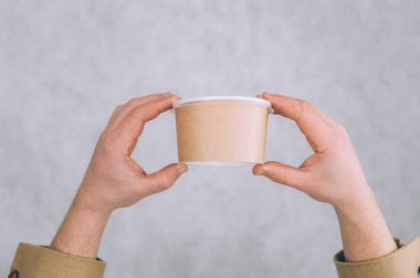 Bir adam arka planda çorba, kahve ve çay için kağıt bardakların maketini tutuyor.