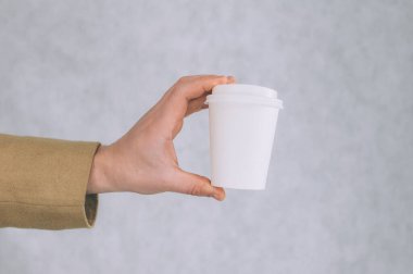 Bir adam, arka planda kahve ve çay için kağıt bardak maketi tutuyor.