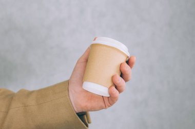 Bir adam, arka planda kahve ve çay için kağıt bardak maketi tutuyor.