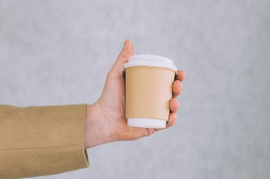 Bir adam, arka planda kahve ve çay için kağıt bardak maketi tutuyor.