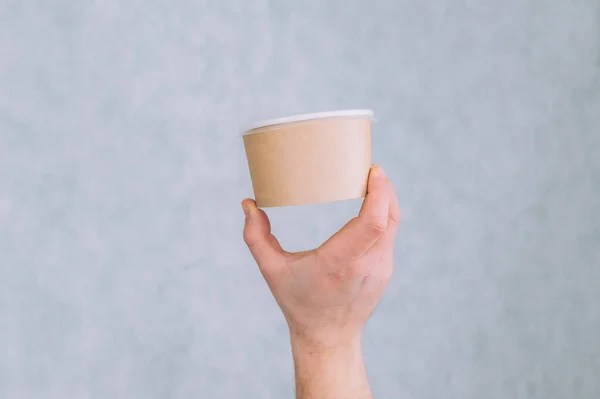 A man holds a mock-up of a paper cup for soup, coffee and tea on a light background
