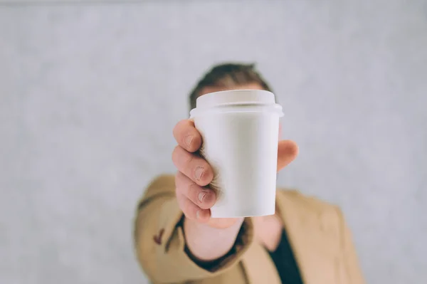 Bir adam, arka planda kahve ve çay için kağıt bardak maketi tutuyor.