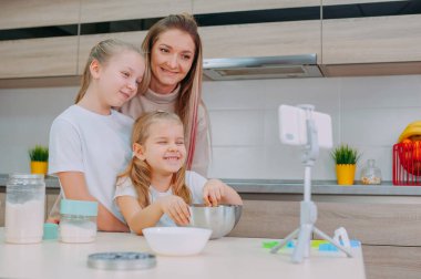 Annem kızlarına mutfakta hamur pişirmeyi öğretiyor. Aile akıllı telefondan aşçılık videosu çekiyor.