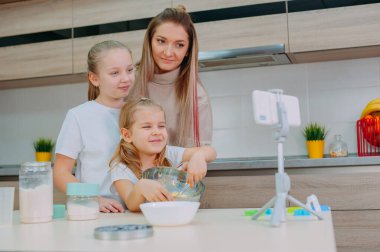 Annem kızlarına mutfakta hamur pişirmeyi öğretiyor. Aile akıllı telefondan aşçılık videosu çekiyor.