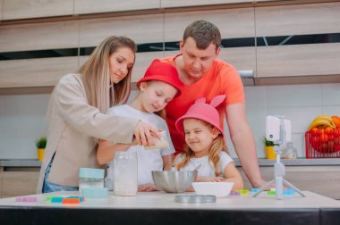 Annem ve babam iki kızıma mutfakta hamur pişirmeyi öğretiyor. Aile akıllı telefondan aşçılık videosu çekiyor.
