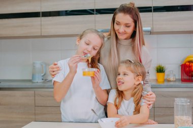 Bir anne ve iki kızı mutfakta yulaf ezmesine bal ekliyor.