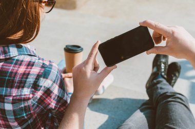 Elinde telefon ve bir fincan kahve olan bir adam temiz havada.