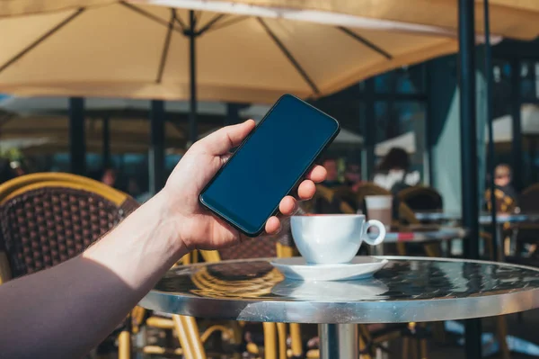 Adam restoranda bir fincan kahvenin arka planında akıllı telefon tutuyor.