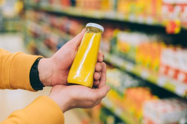 Dükkandaki bir adam elinde bir kutu portakal suyu tutuyor.