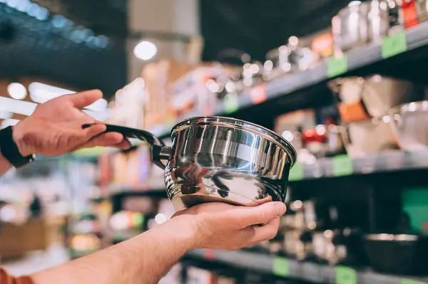 Dükkanda bir adam yeni bir tencere seçer.