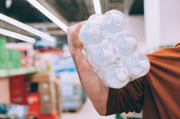 Dükkanda bir adam temiz ve şeffaf bir şişe su tutuyor.