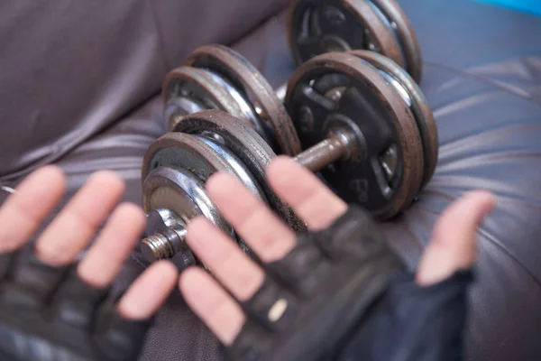 Old rusty dumbbells with hands wearing old worn gloves in the foreground