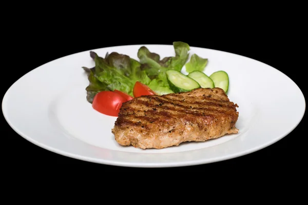 Photo of a pork stake on a white plate with a cucumber, tomato a — Stock Photo, Image