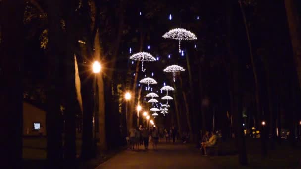 Video's van mensen in het steegje en de Led-lampen in de vorm van paraplu's in het park in de avond wandelen — Stockvideo